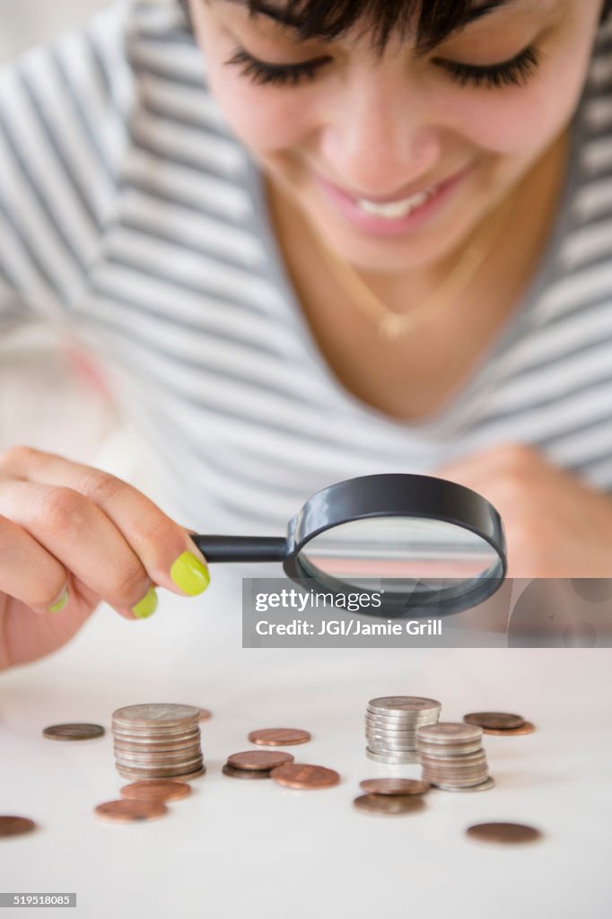 Mixed race woman examining stacks of coins with magnifying glass