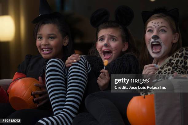 girls in costumes watching scary movie together on halloween - halloween kids stockfoto's en -beelden