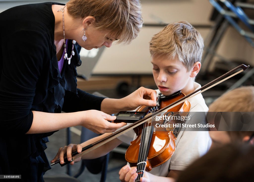 Caucasian teacher tuning students instrument in music class