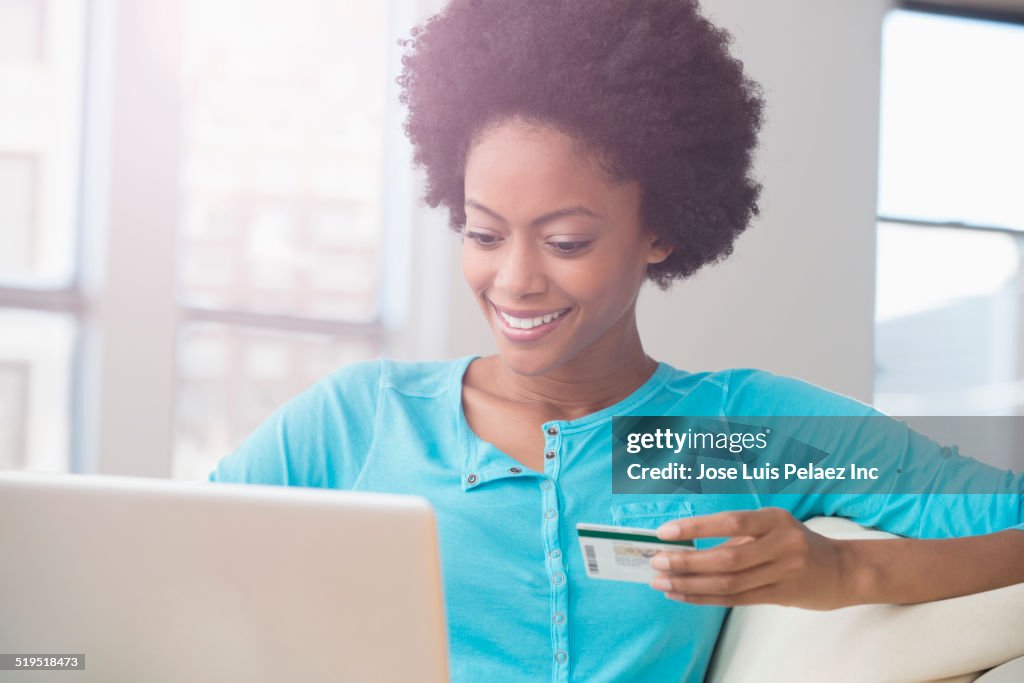 African American woman shopping on laptop with credit card on sofa
