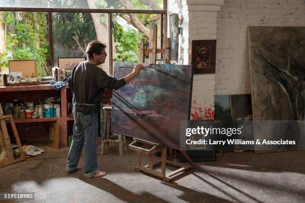 hispanic artist painting in studio - schürze mann rückansicht stock-fotos und bilder