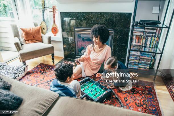 mixed race family playing foosball on living room floor - fashionable mom stock pictures, royalty-free photos & images