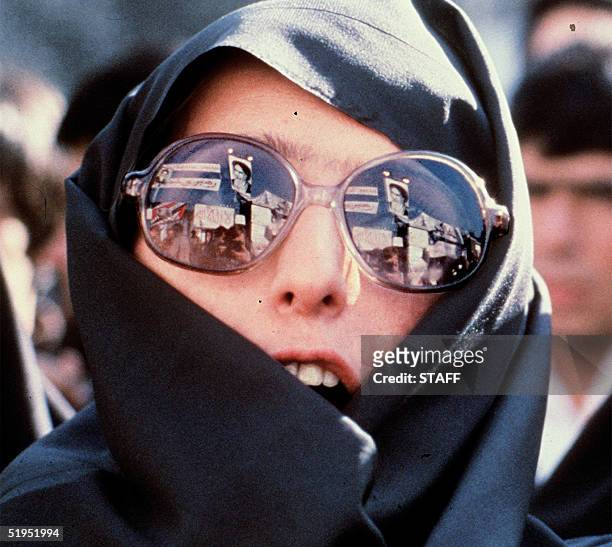 Heavily veiled Iranian woman with modern glasses in which slogans and Ayatollah Khomeini' s portrait are reflected demonstrates outside of the US...