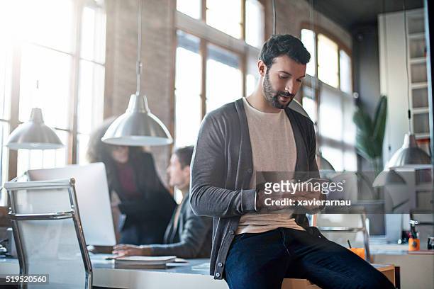 uomo d'affari controlla il mobile telefono seduto sulla sua scrivania - portable information device foto e immagini stock