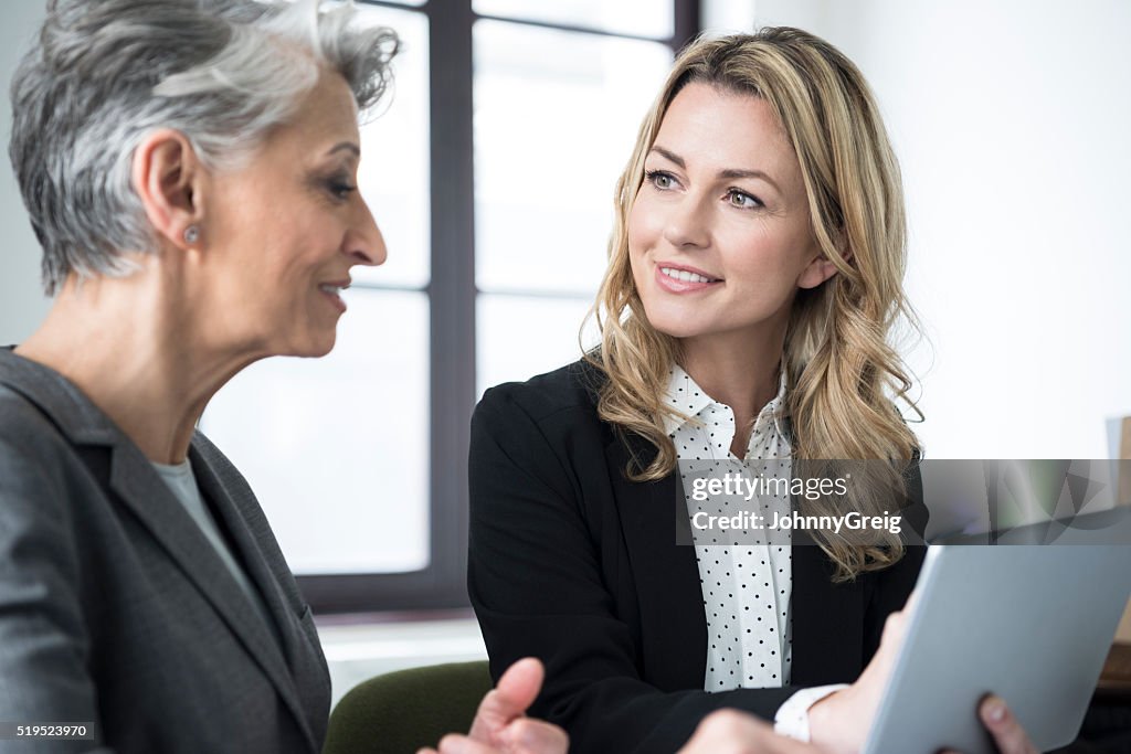 Mid adult woman with tablet smiling at mature colleague
