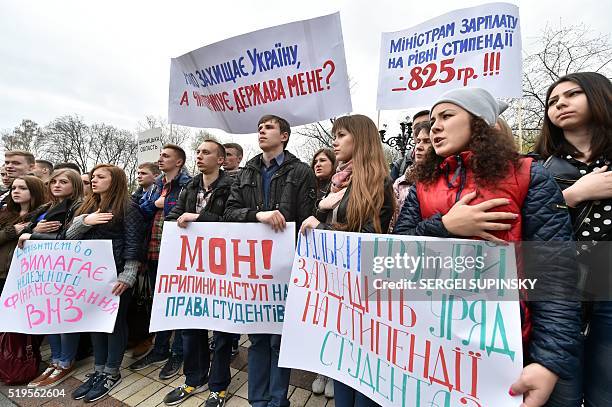 Ukrainian university students hold their hands over their hearts and placards reading "We demand scholarship indexing", "Hands off of student...