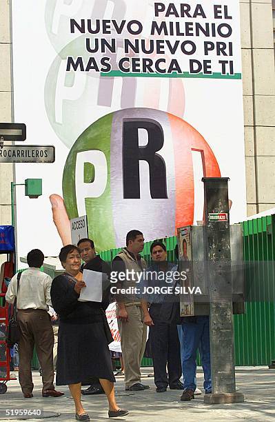 Group of people wait in front of a public phone in front of a poster that promotes the Institutional Revolutionary Party for the Mexico's Political...