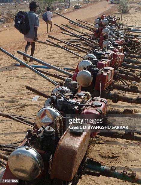 Indian children, tsunami survivors, walk past a queue of recovered engines used in the fishing boats as they go to school in Periyanmmeli area,...