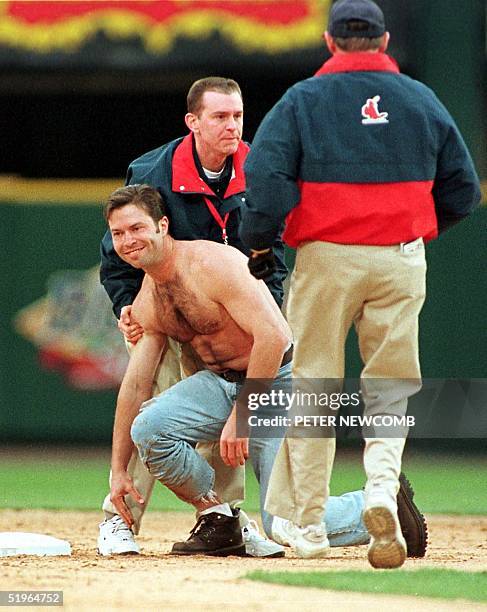 Shirtless fan is grabbed and escorted off the field by two ushers after rushing onto the field and sliding into second base during the top of the...