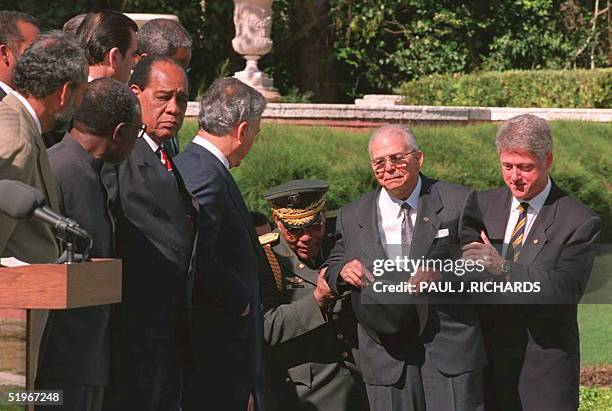 President Bill Clinton and a Dominican officer help Dominican Republic President Joaquin Balaguer to climb onto a podium set for the group photo...