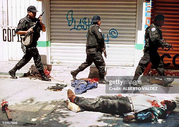 Police walk past the body of a man killed during exchange of gunfire between rival factions, 18 August, 2000 in the streets of Chimalhuacan, some 45...
