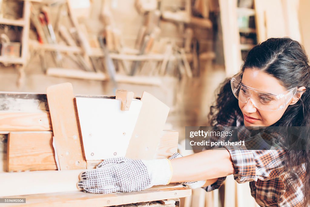 Female carpenter planing wood with at work site