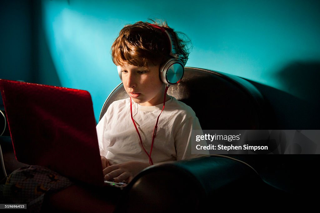 Boy on laptop with headphones in dark room