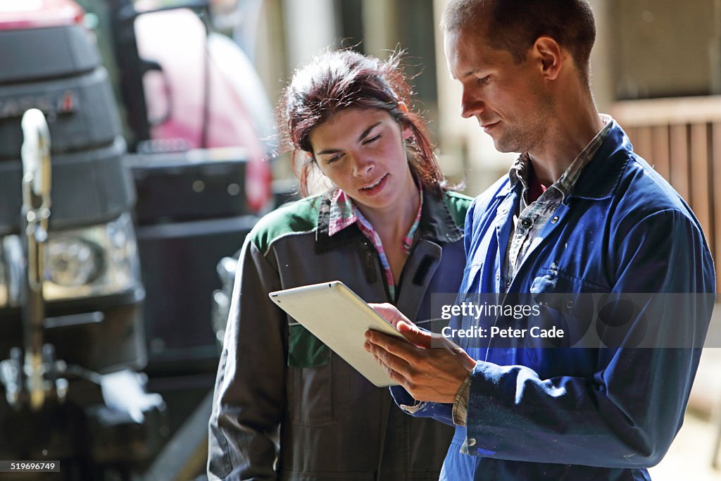 Famers couple looking at tablet . farm and tractor