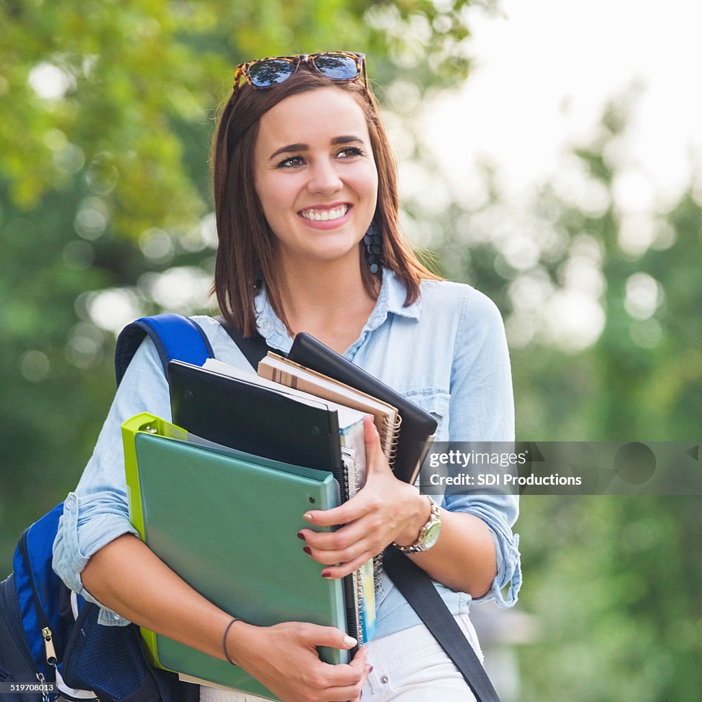 Happy college student walking to class with stack of books