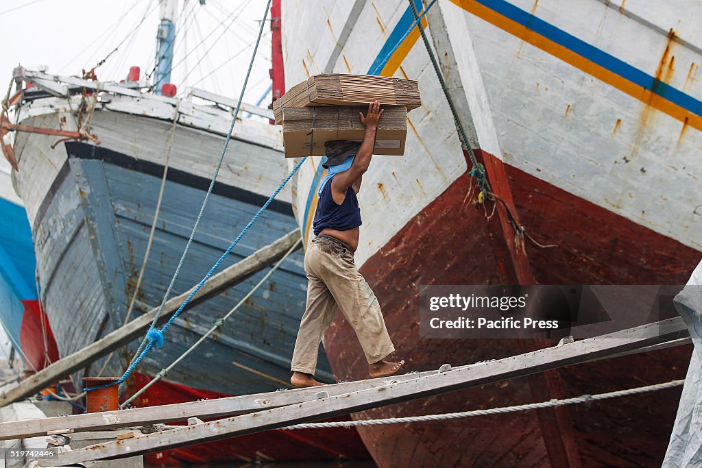 A worker carries cardboard boxes onto a ship for transport...