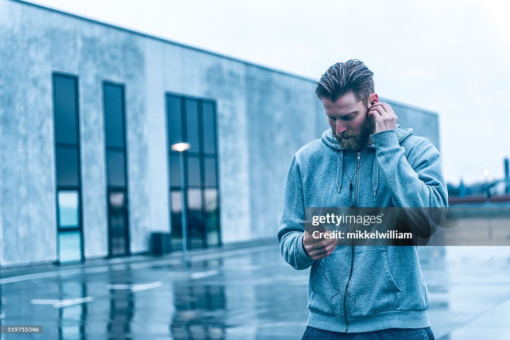 Man with beard listens to music on smart phone outside