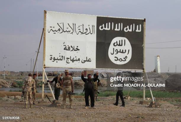Iraqi government forces gather under a billboard bearing slogans of the Islamic State group and its trademark flag, in the town of Heet, in Iraq's...