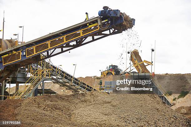 Dump truck unloads materials as a mine feed conveyor operates at the MZI Resources Ltd. Keysbrook mineral sands mine in Keysbrook near Perth,...