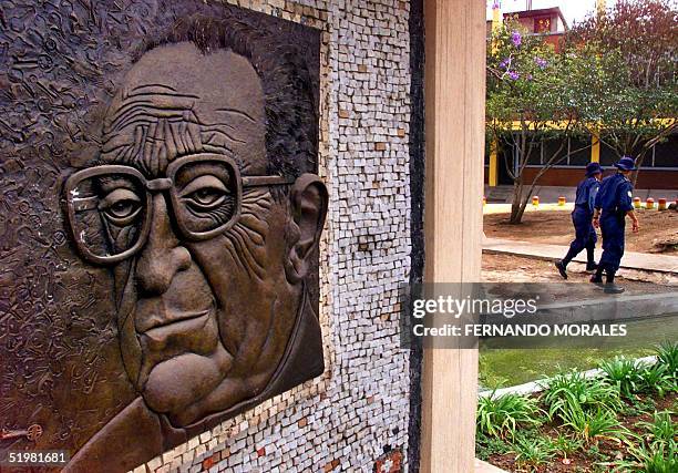 Two police officers walk 20 March 2001 by a bronze sculpture of Guatemalan bishop Juan Gerardi outside the parochial house where he was murdered 26...