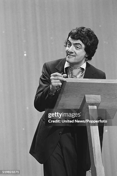 English comedian and actor, Rowan Atkinson performs at a lectern on stage at the Palladium in London during rehearsals prior to his performance on...