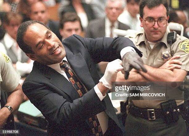 Double murder defendant O.J. Simpson puts on one of the bloody gloves as a Los Angeles Sheriff's Deputy looks on during the O.J. Simpson murder trial...