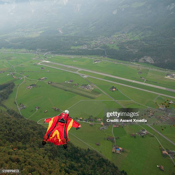 wingsuit flyer, mid-air descent from cliff, valley - wing suit stock pictures, royalty-free photos & images