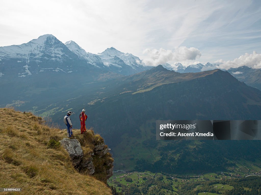 Wingsuit flyers stand at edge of cliff, valley