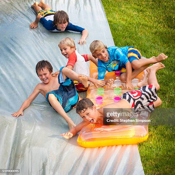 boys tumbling down backyard downhill slip n slide - backyard water slide stock pictures, royalty-free photos & images