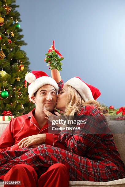 young couple kissing under mistletoe - mistletoe kiss stockfoto's en -beelden