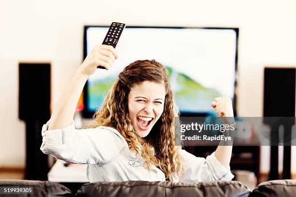 my team's winning! pretty tv spectator cheers on her side - yes stockfoto's en -beelden