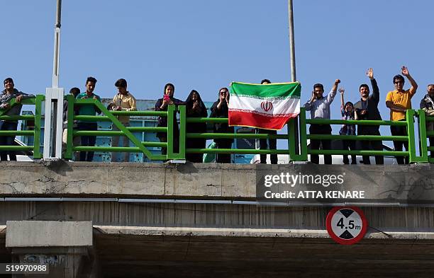 Iranians stand on a bridge waving their national flag and cheering as they support Iranian and foriegn runners competing in Iran's first internation...