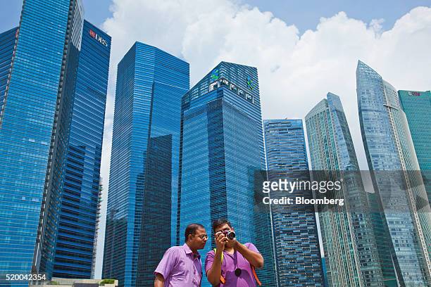 Tourists look at the screen on a digital single lens reflex camera in front of commercial buildings at the Marina Bay Financial Centre in Singapore,...