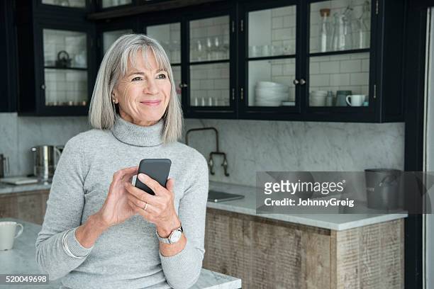 senior woman using smartphone in modern kitchen - white polo stock pictures, royalty-free photos & images