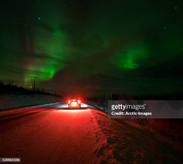 car stopped on road beneath the aurora borealis - rear light car stock-fotos und bilder