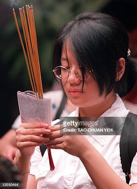Holding incense sticks and her examination ID, a female high school student prays at Lung Shan Temple 30 June for good luck at the three-day college...