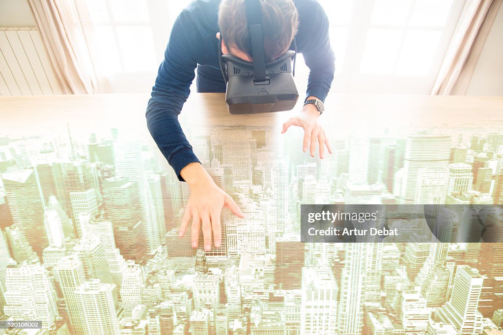 Guy interact with virtual reality headsets from the living room home touching and moving a hologram of a city view over the table.