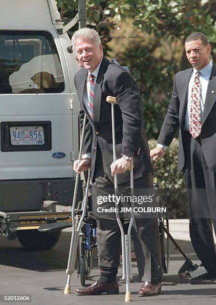 President Bill Clinton , accompanied by a Secret Service agent, walks with the aid of crutches 23 March upon arrival at the White House after...