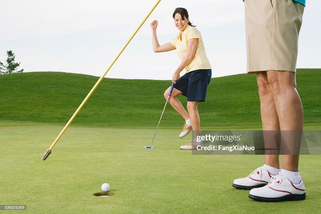 Woman hitting golf ball into the hole