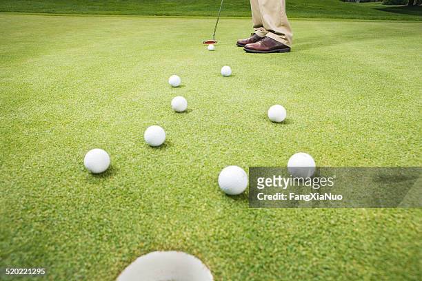 golfer hitting ball through group of golf balls, low section - golf putter stock pictures, royalty-free photos & images