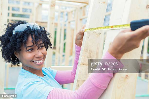 african american woman measures board on charity house - habitat for humanity stock pictures, royalty-free photos & images