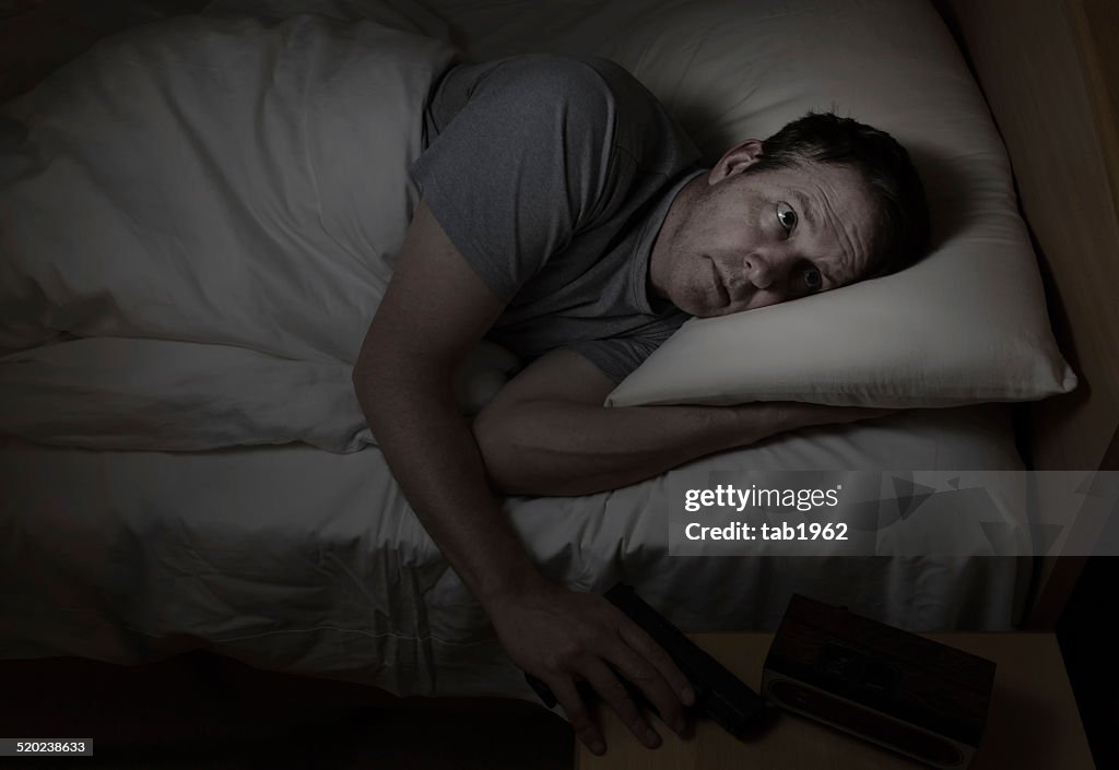 Besorgt Mann greift gun aus Nachttisch, während im Bett