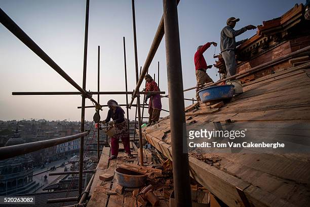 Construction workers, experienced in traditional Nepali style architecture, are standing on a scaffold and rebuild the top of the major Taleju temple...