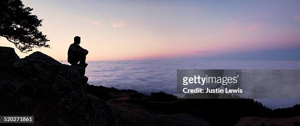 solo man sits on mountain top, silhouette, sunrise - one man only stock pictures, royalty-free photos & images