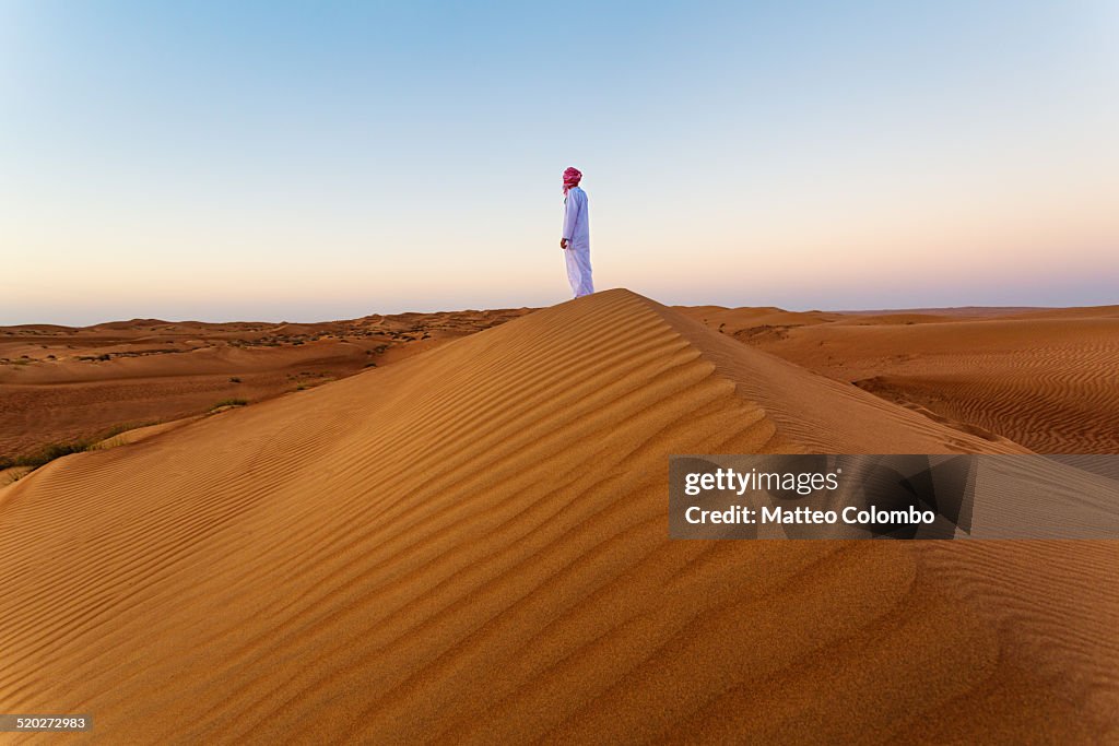 Omani man looking at sunrise in the desert, Oman