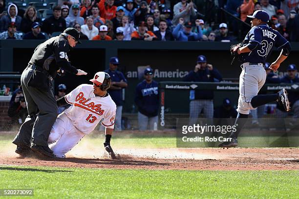 Manny Machado of the Baltimore Orioles collides with home plate umpire Dana DeMuth after scoring on a wild pitch by Erasmo Ramirez of the Tampa Bay...