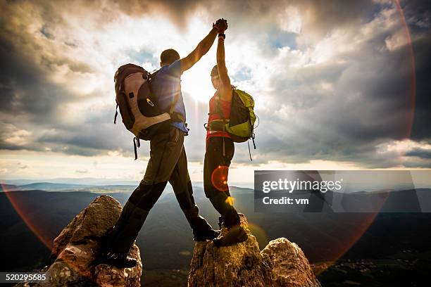 pareja en la cima de una montaña agitación planteado las manos - mountaineering fotografías e imágenes de stock