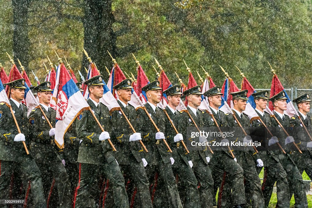 Soldiers marching on a military parade carrying flags in downpour.