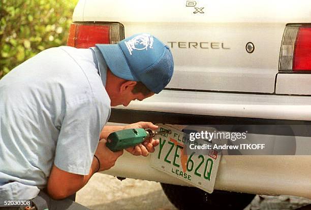 Juan Alberto, a mechanic at Alamo Car rental, removes an old license plate 07 April 1993 that begins with a "Y" and reads "Lease" at the bottom to...