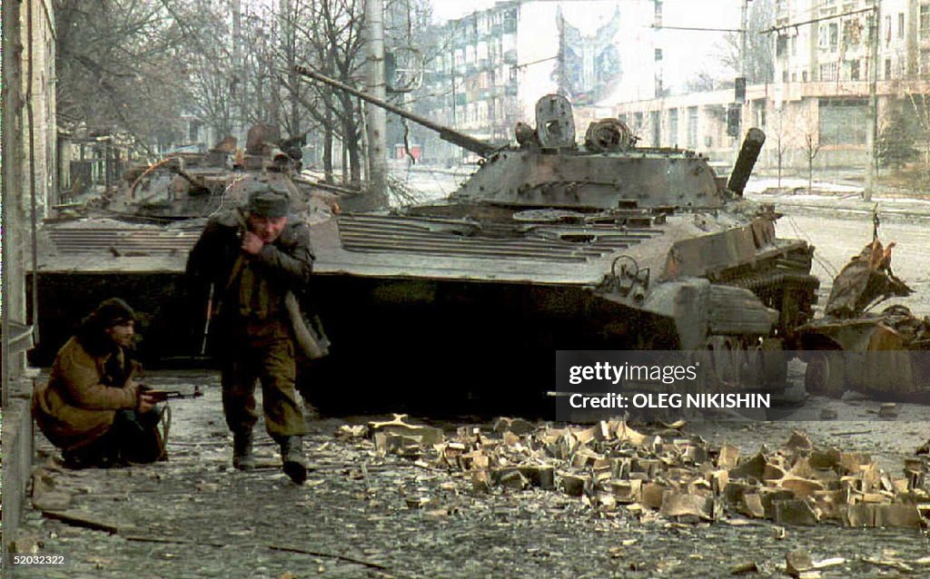 A Chechen fighter runs for cover as another hides